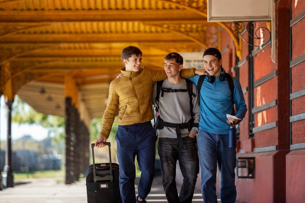 Tres chicos jóvenes viajando en tren en una estación