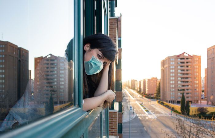 Mujer mirando por la ventana con mascarilla 