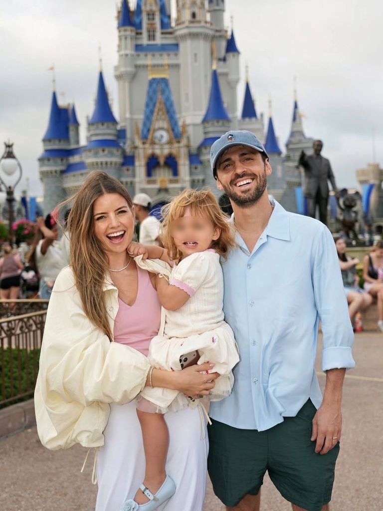 Hombre y mujer con una niña en Disneyland, sonriendo para la foto.