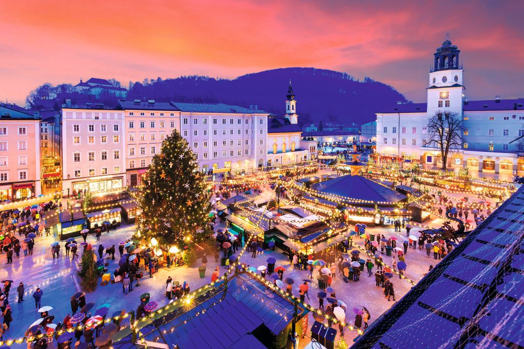Vista aérea de una plaza con un mercado navideño, luces y gente. No se detectan celebridades.
