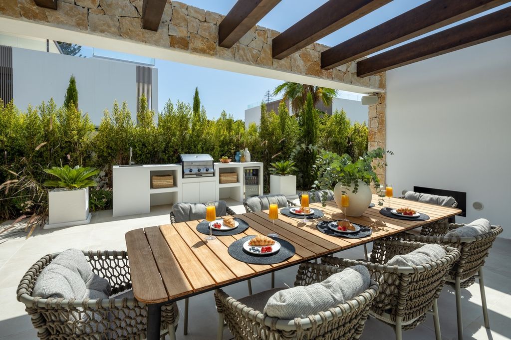 Comedor al aire libre, bajo una pérgola, y cocina de exterior