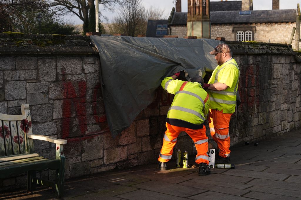 Los operarios, limpiando el grafiti del templo donde se ha celebrado la misa