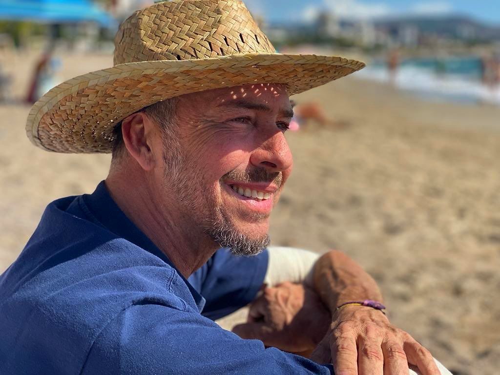 Primer plano de Nacho Palau posando en la playa con un sombrero de paja