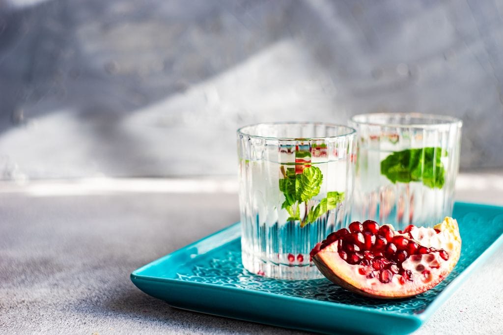 Bandeja con vasos de agua, hojas de menta y granada