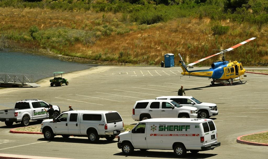 Sheriff department vehicles and a helicopter sit in a parking lot along with emergency workers at Lake Piru