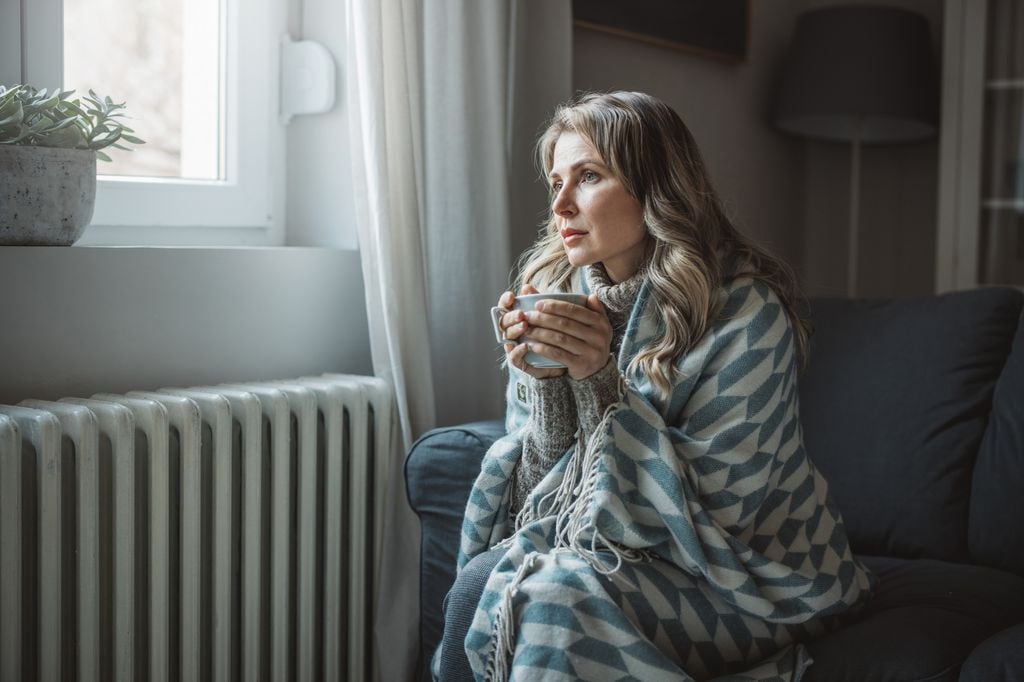 mujer con frío en casa, con una manta y una taza de café