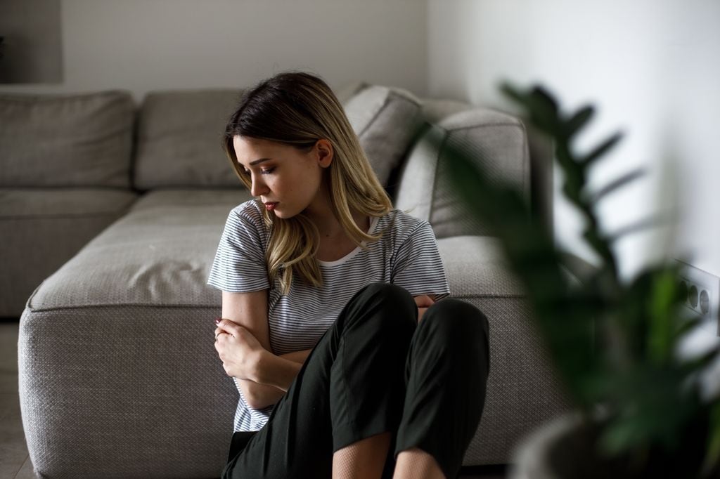 mujer triste en casa sentada junto al sofá