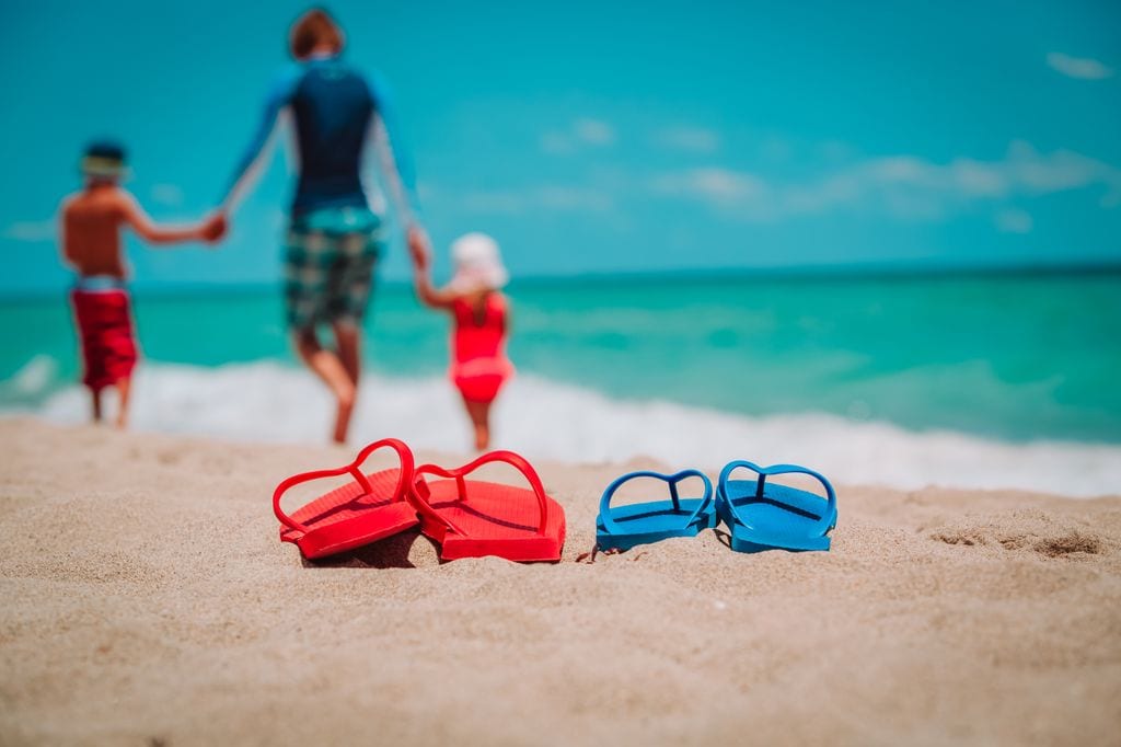 Padre paseando con sus hijos por la playa con chanclas en primer plano