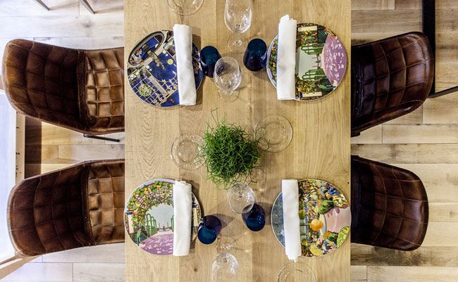 Mesa de comedor con sillas de cuero, platos decorados, copas y cubiertos.