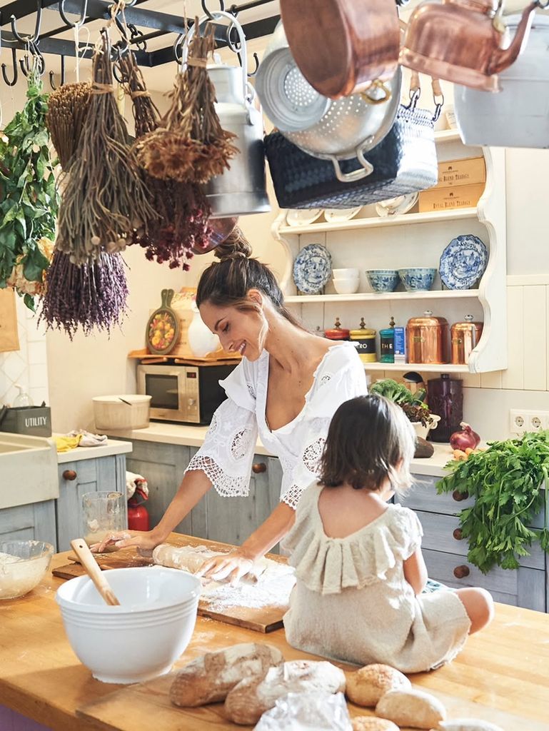 Ariadne Artiles en su cocina amasando pan con su hija sentada en la mesa de madera