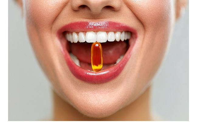 Mujer con la boca abierta sosteniendo una pastilla naranja entre sus dientes.