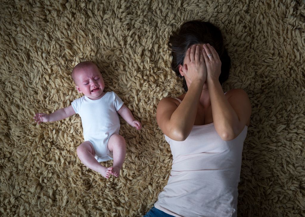 Madre con depresión posparto con su bebé tapándose la cara