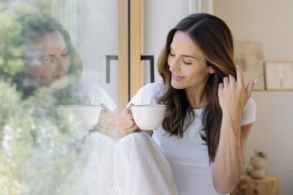 Mujer mirando por la ventana mientras se toma un café