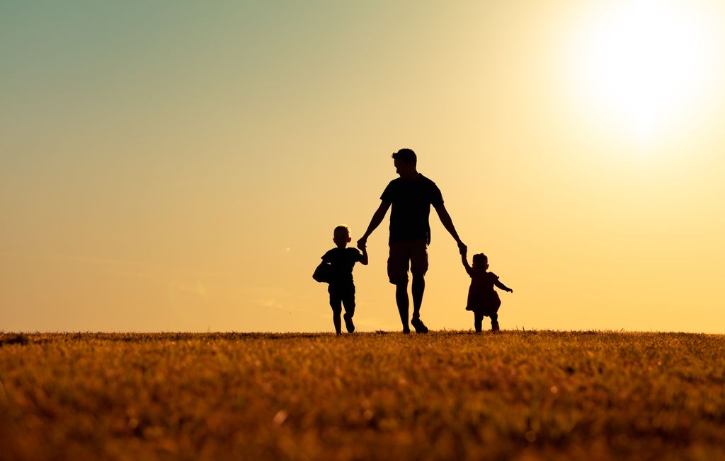 Padre en un paisaje de puesta de solo con sus dos hijos 