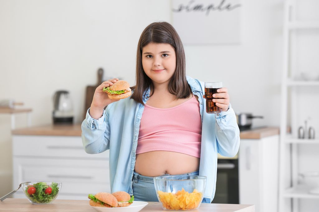Niña con sobrepeso con comida basura en las manos