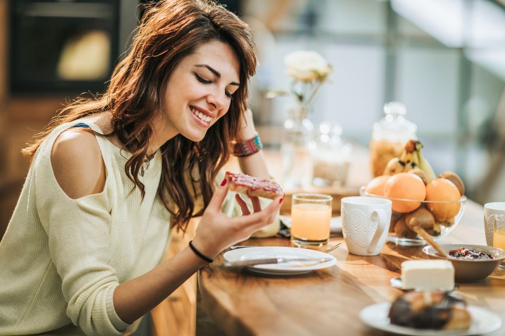 mujer sonriente desayunando pan con mermelada
