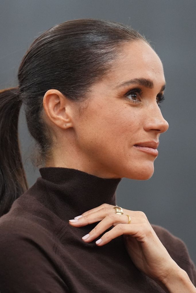 Primer plano de Meghan Markle con manicura rosa clara y jersey de cuello vuelto granate
