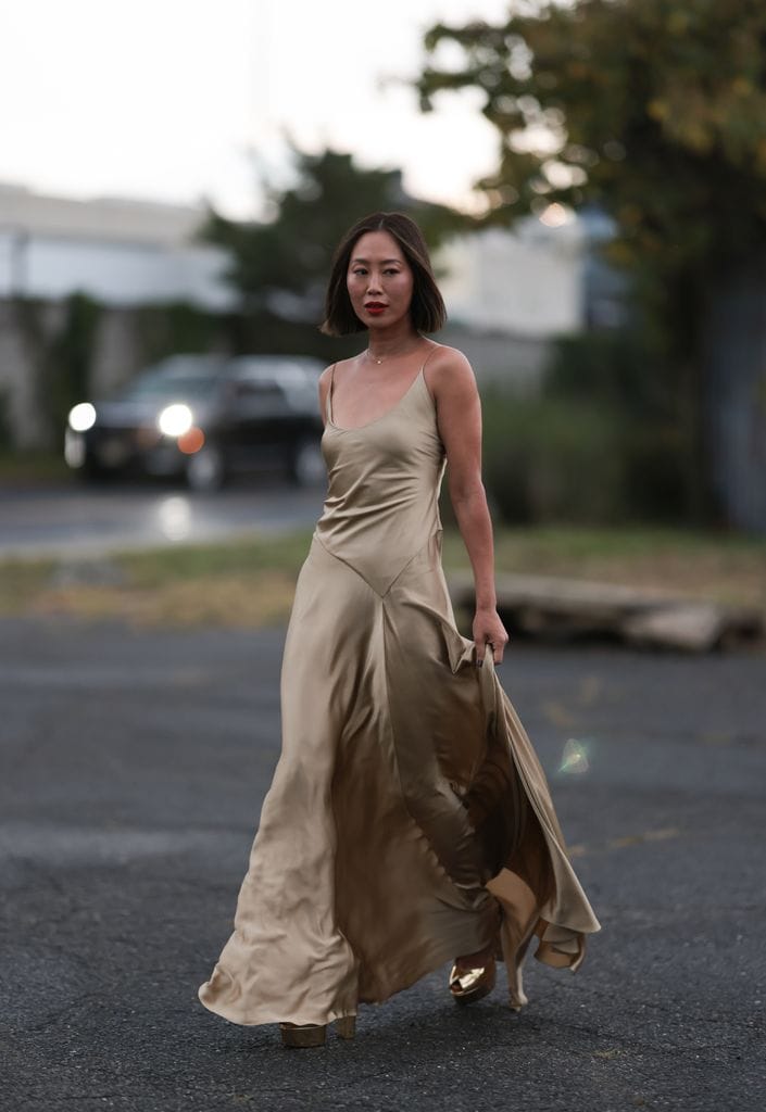Aimee Song es vista fuera del desfile de Ralph Lauren luciendo un collar dorado con un diamante, dorado, fluido, de seda, vestido largo de Ralph Lauren sin mangas y tacones dorados de meseta brillante de Ralph Lauren el 08 de septiembre de 2023 en la ciudad de Nueva York
