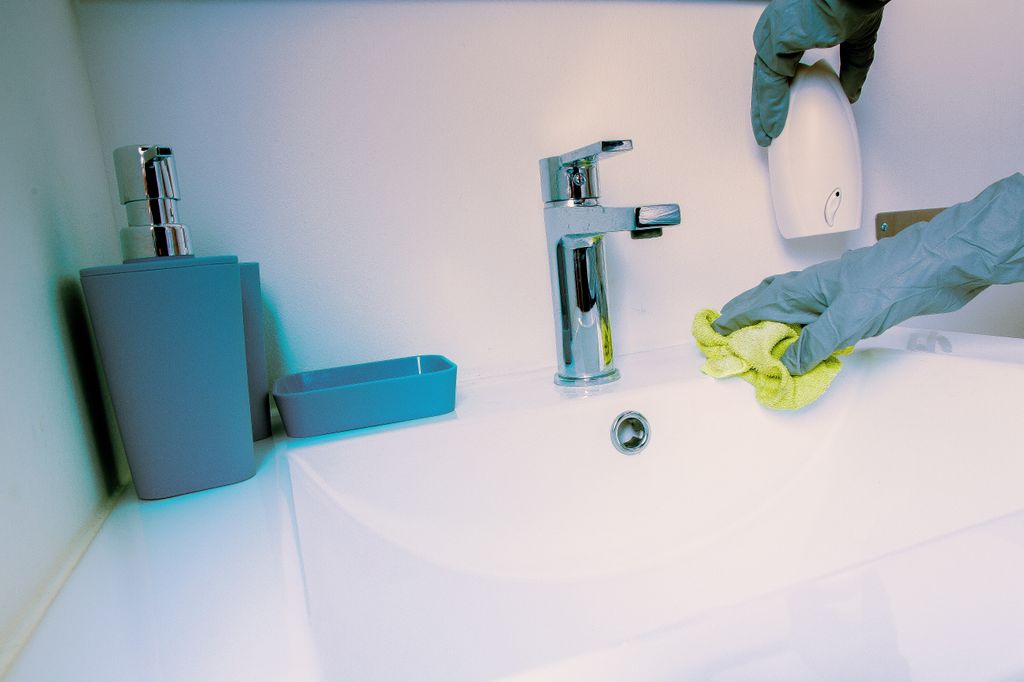 Desinfección del baño aplicando lejía con un paño y protegidos con guantes