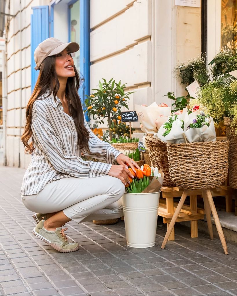 Mujer arrodillada junto a florero, seleccionando flores en mercado al aire libre.