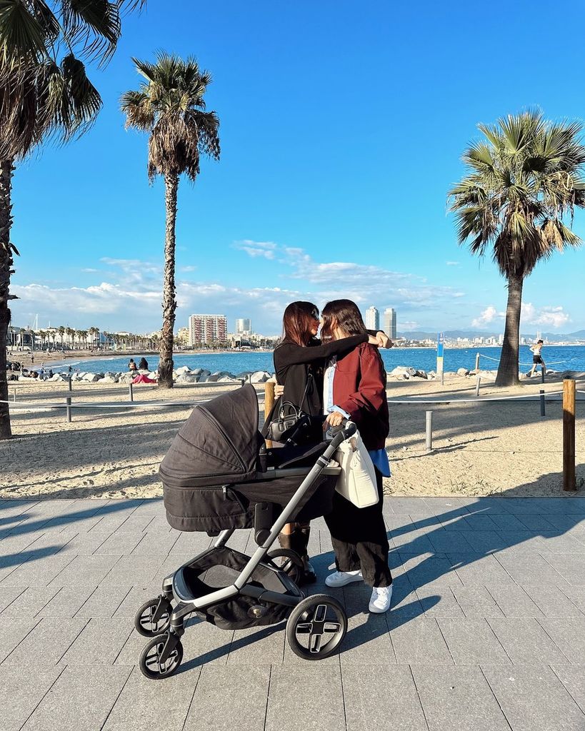 Plano entero de Alba Paul y Dulceida dándose un beso paseando a su bebe