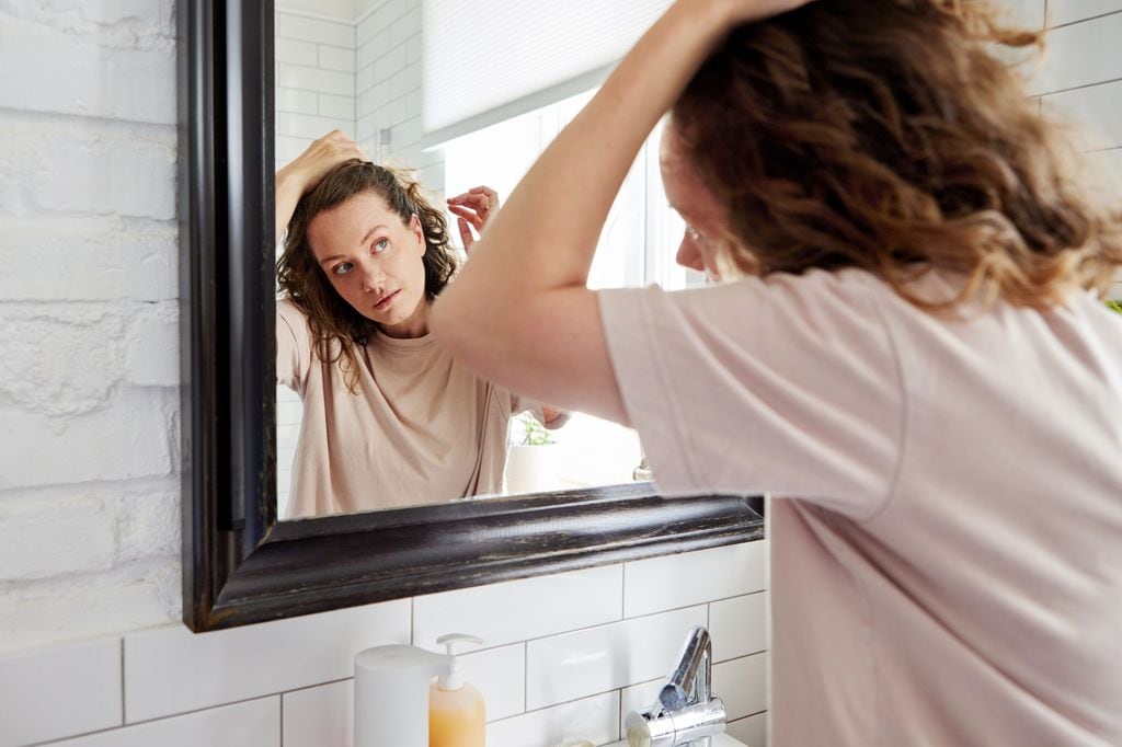 mujer mirándose frente al espejo, mientras se toca el pelo