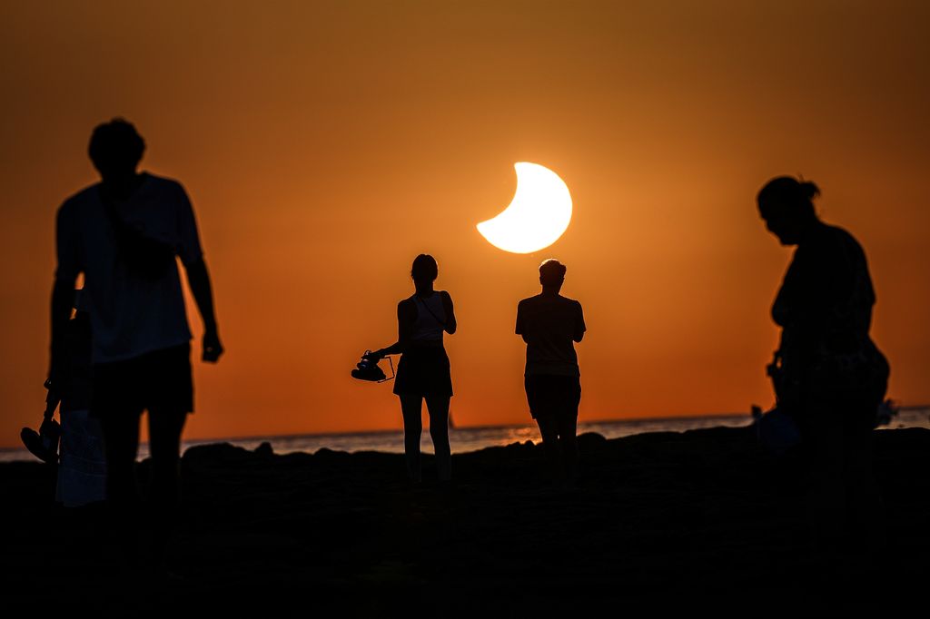 Varias personas contemplan el avance de la Luna sobre el Sol desde la costa de Cádiz