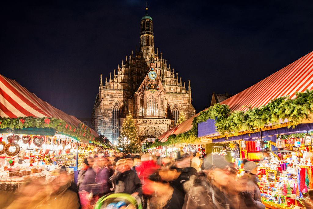 Multitud en el célebre mercado navideño de Núremberg, uno de los más antiguos y visitados del mundo, con la Iglesia de Nuestra Señora iluminada al fondo