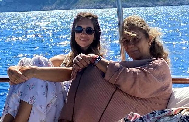 Dos mujeres, una con gafas de sol, sentadas en un barco, una abrazando a la otra.