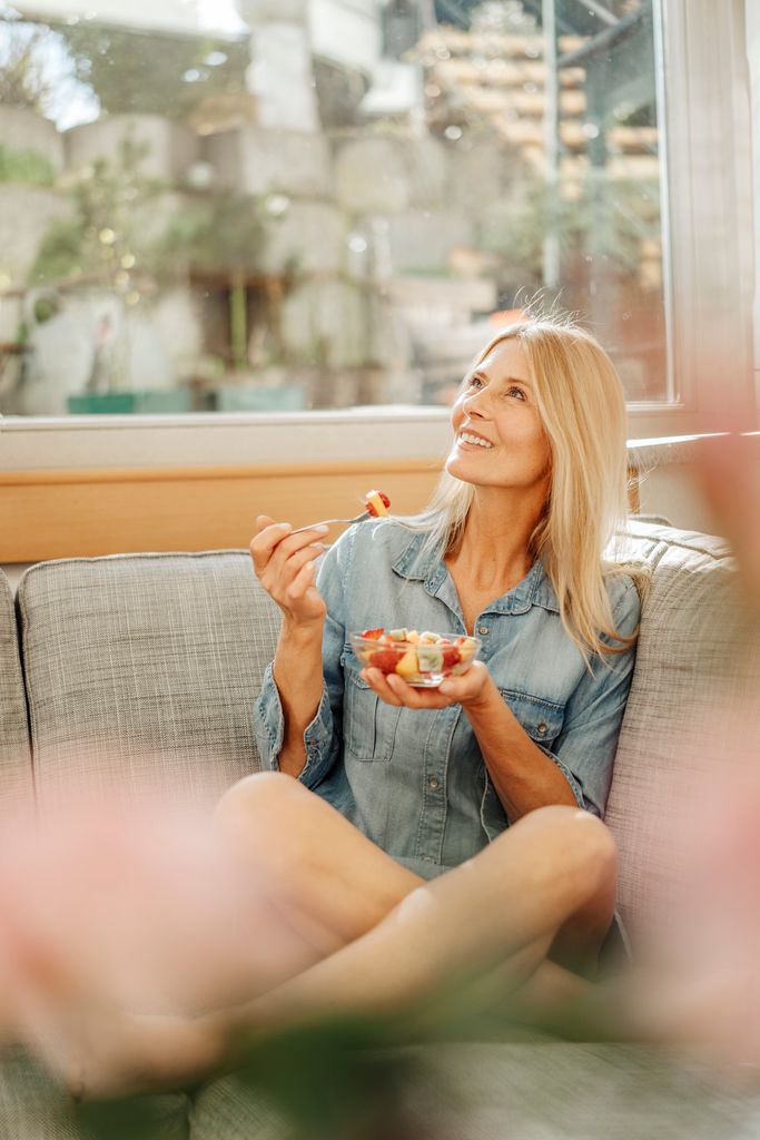 Una mujer sonriente con un bol de fruta en su salón