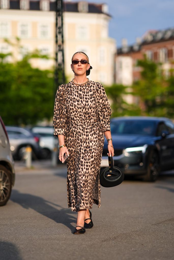 COPENHAGEN, DENMARK - AUGUST 7: A guest wears black sunglasses, black scrunchie, brown necklace, cream and black leopard pattern/print long sleeve maxi dress, gold bracelets, gold rings, black leather bag, shiny black ballerina flats leather shoes, outside Baum und Pferdgarten, during the Copenhagen Fashion Week Spring/Summer 2024-2025 on August 7, 2024 in Copenhagen, Denmark. (Photo by Edward Berthelot/Getty Images)