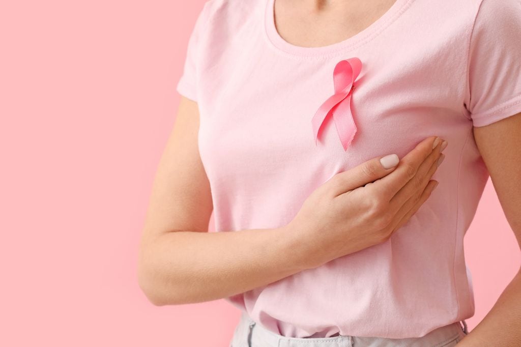 mujer palpándose el pecho, con una camiseta rosa con un lazo