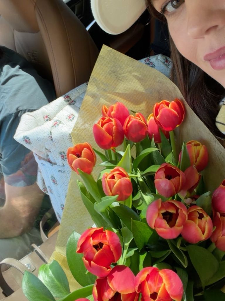 Isabelle en una foto con su marido al volante y un ramo de tulipanes