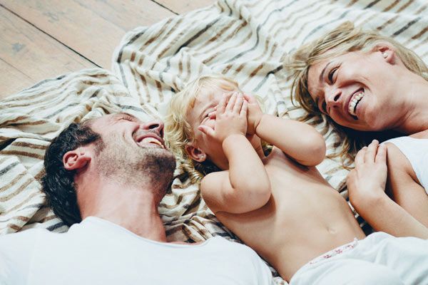 Un hombre, una mujer y un niño ríen juntos en una manta en el suelo.