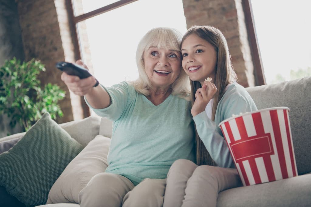 Niña viendo con su abuela una película en su casa