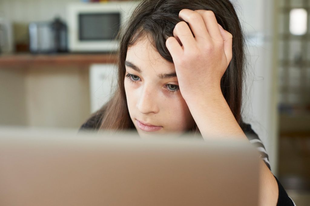 Adolescente abatida mirando el ordenador por ciberbullying