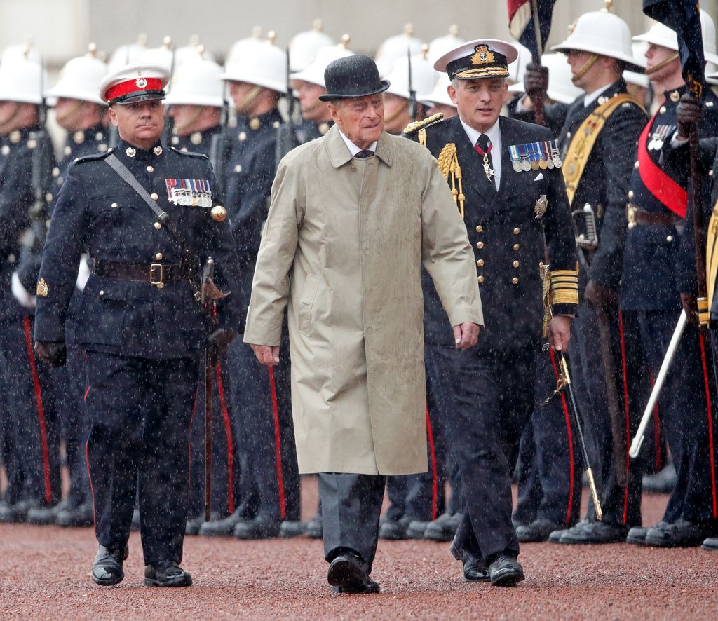 El Príncipe Felipe, Duque de Edimburgo, camina bajo la lluvia con oficiales militares.
