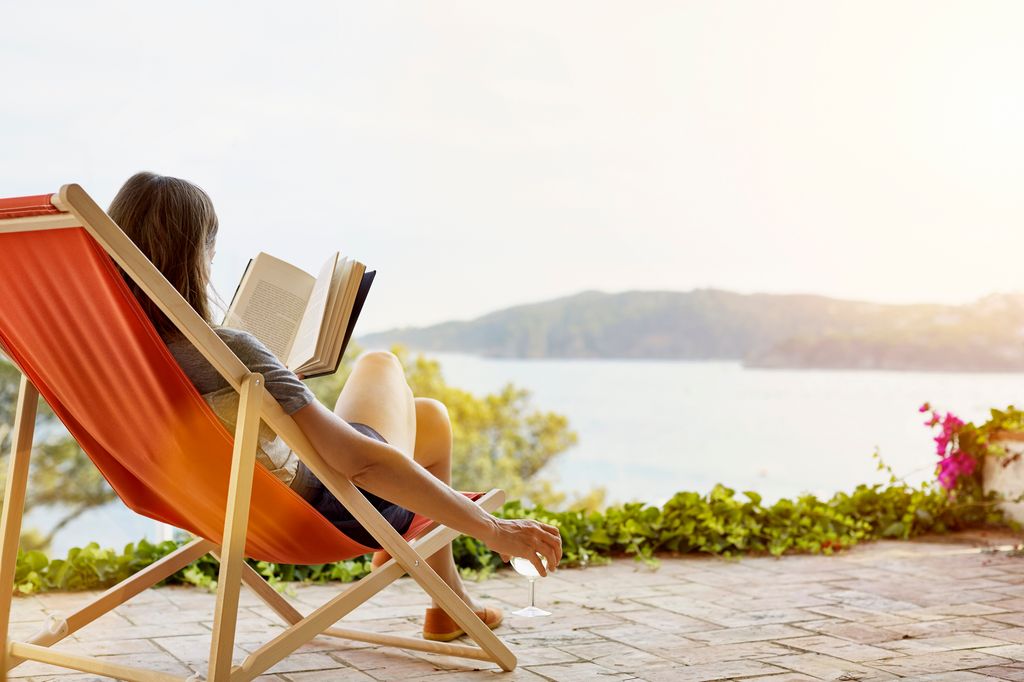 Mujer leyendo un libro mientras se relaja en una tumbona en el patio trasero.