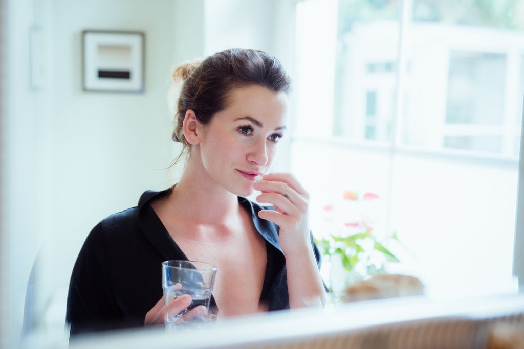 Mujer tomando vitaminas y suplementos alimenticios frente al espejo