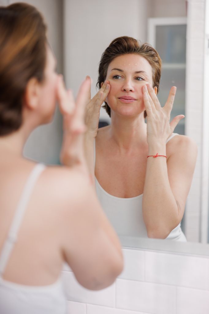 Rostro de mujer madura mirándose al espejo mientras se estira la piel desde las mejillas