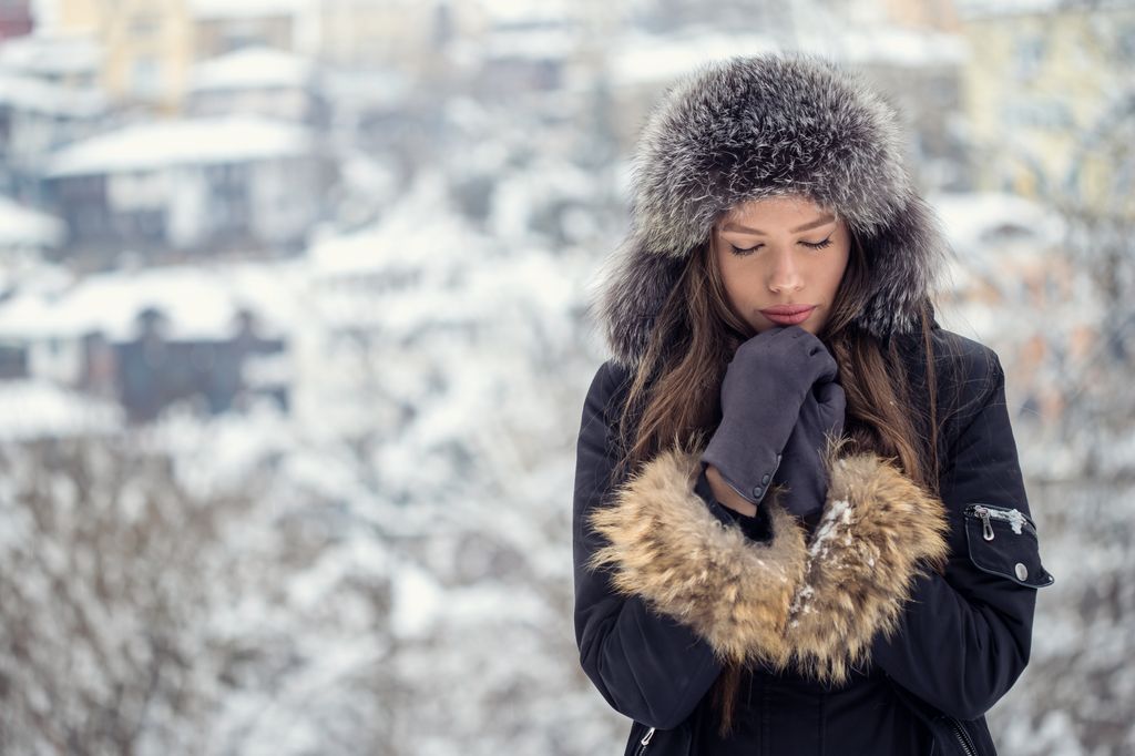 Pretty woman warming hands with breath on cold winter day in nature.