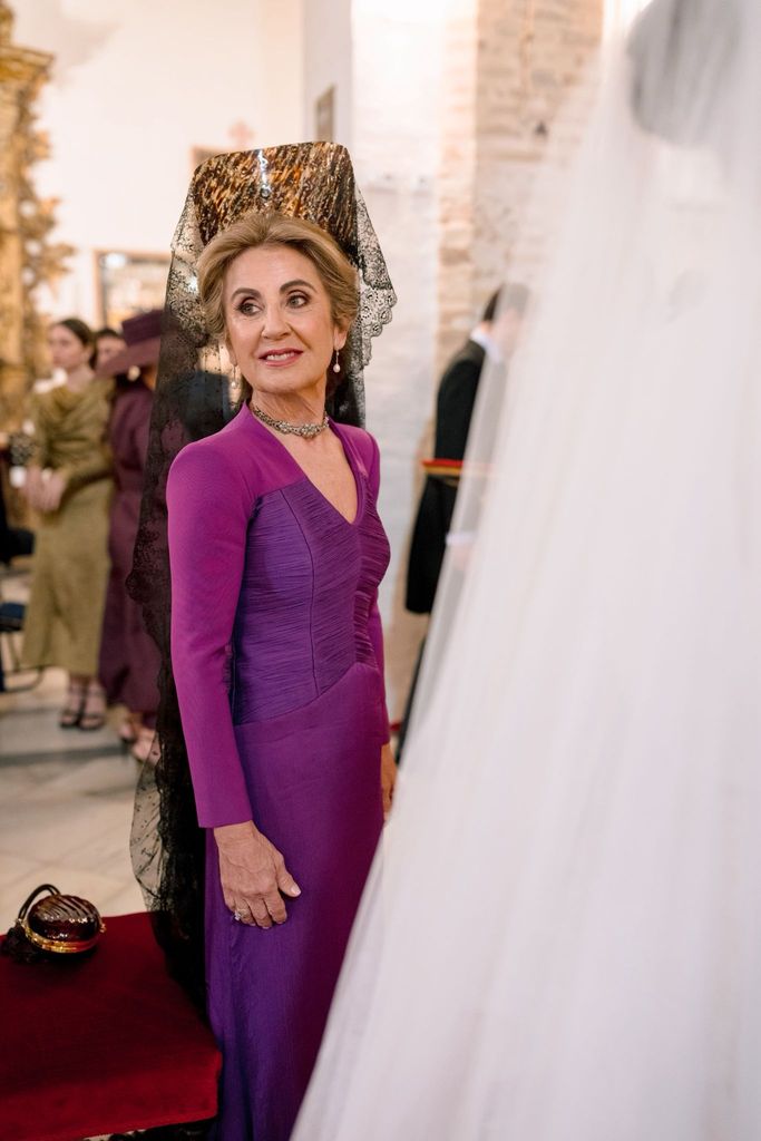 Madrina de boda con mantilla de chantilly, vestido morado y gargantilla