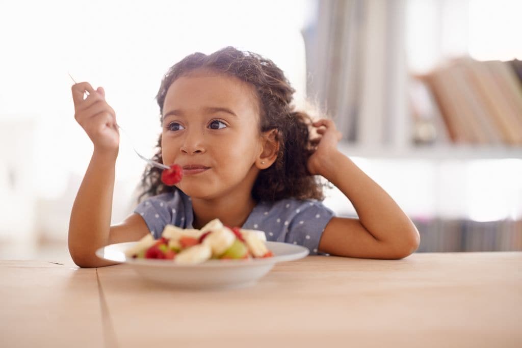 Niña tomando fruta sentada a la mesa