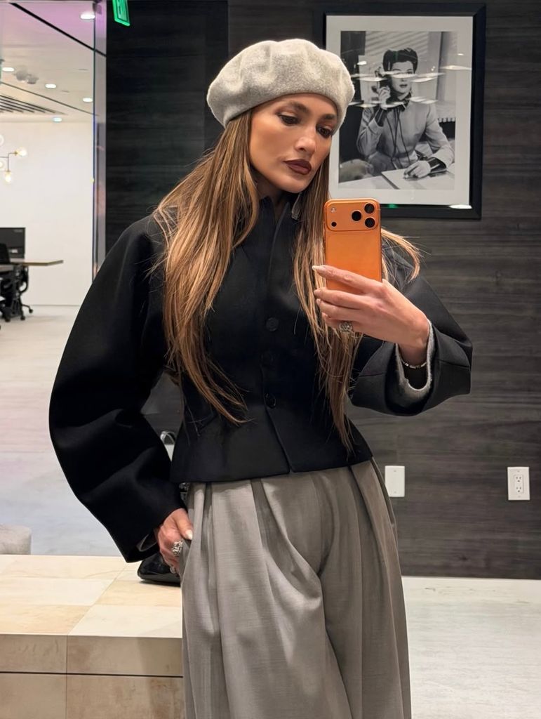 Jennifer Lopez con boina gris, labios marrones y manicura afterglow, en un look parisino contemporáneo.