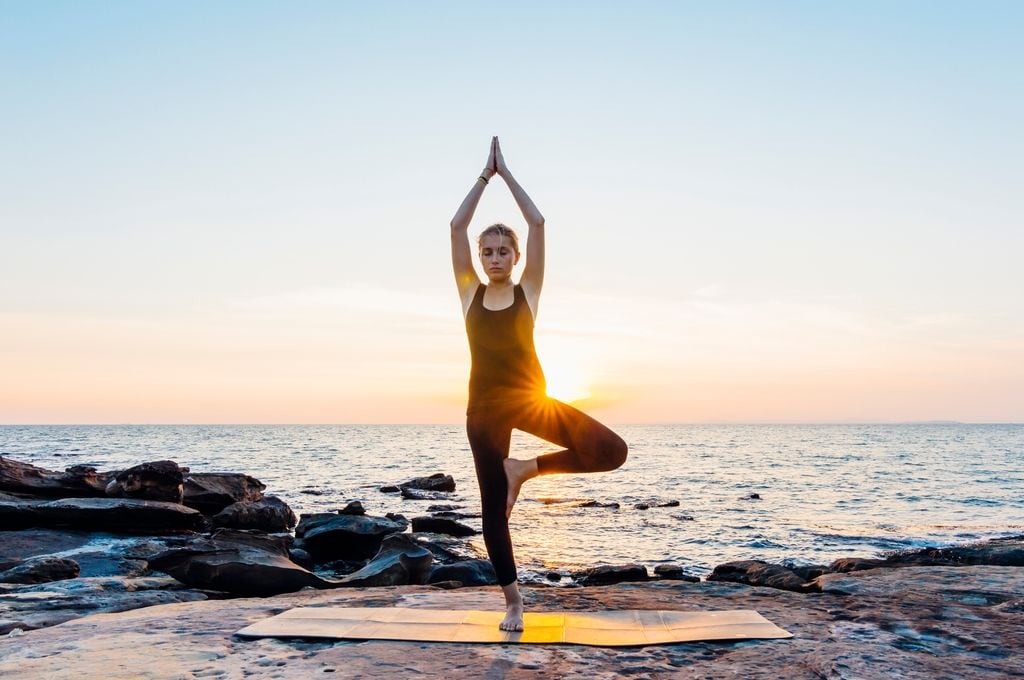 mujer haciendo la postura del árbol de yoga al aire libre, junto al mar