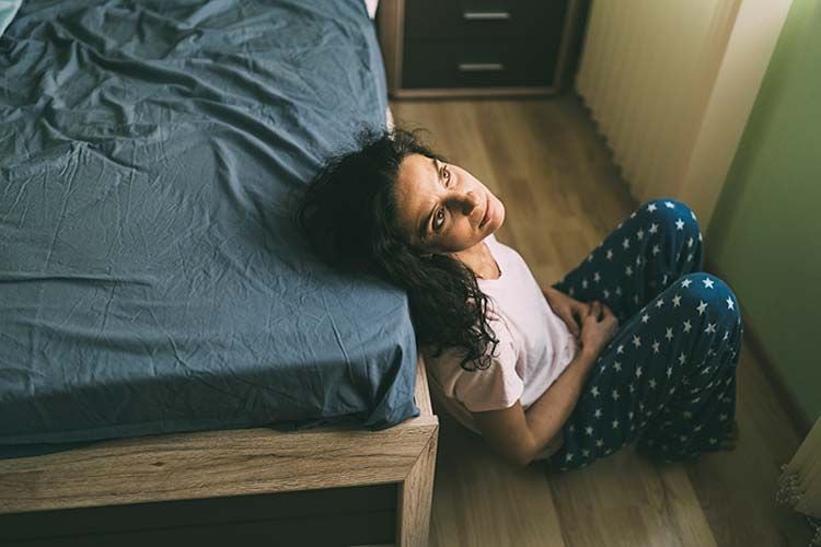 Mujer sentada en el suelo y apoyada en la cama en actitud pensativa