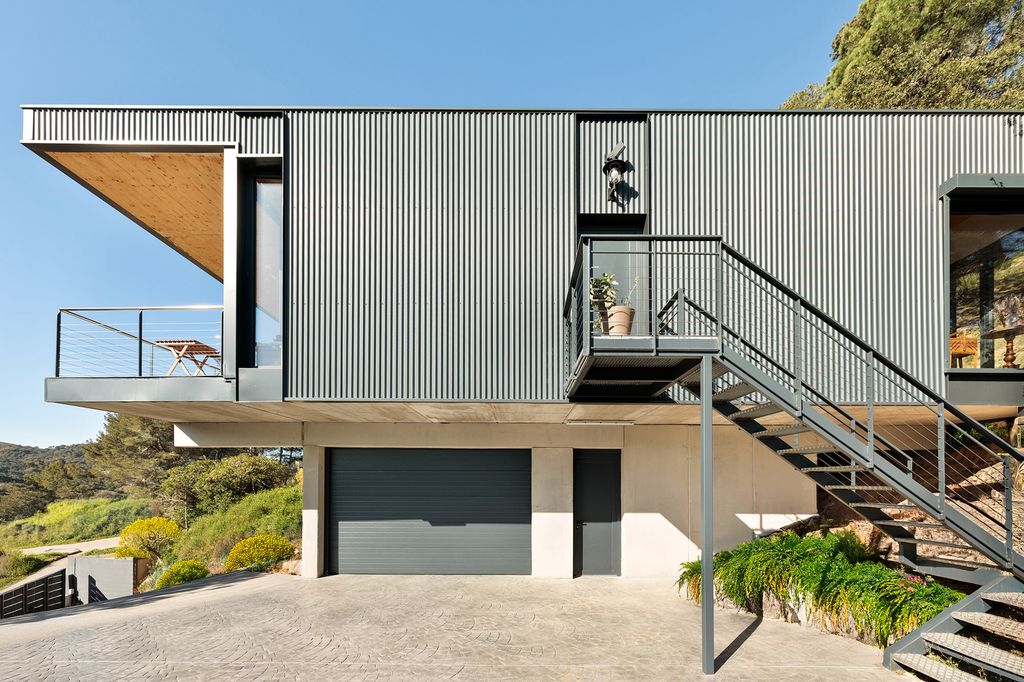 Casa de dos plantas con garaje, fachada metálica negra, escalera y terraza