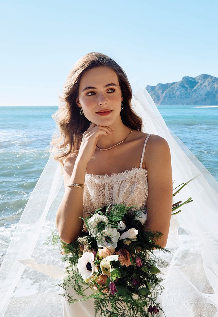 LA SONRISA DE LA NOVIA
La delicadeza del encaje acompaña a nuestra novia, que en esta imagen posa, radiante, con top de encaje, de Lorena Formoso; falda, de Candelas y Felipa; velo, de Rosa Clará; collar rivière, de Rabat; pendientes, de Leandra Studio, y anillos y pulseras brillantes, de Suarez.