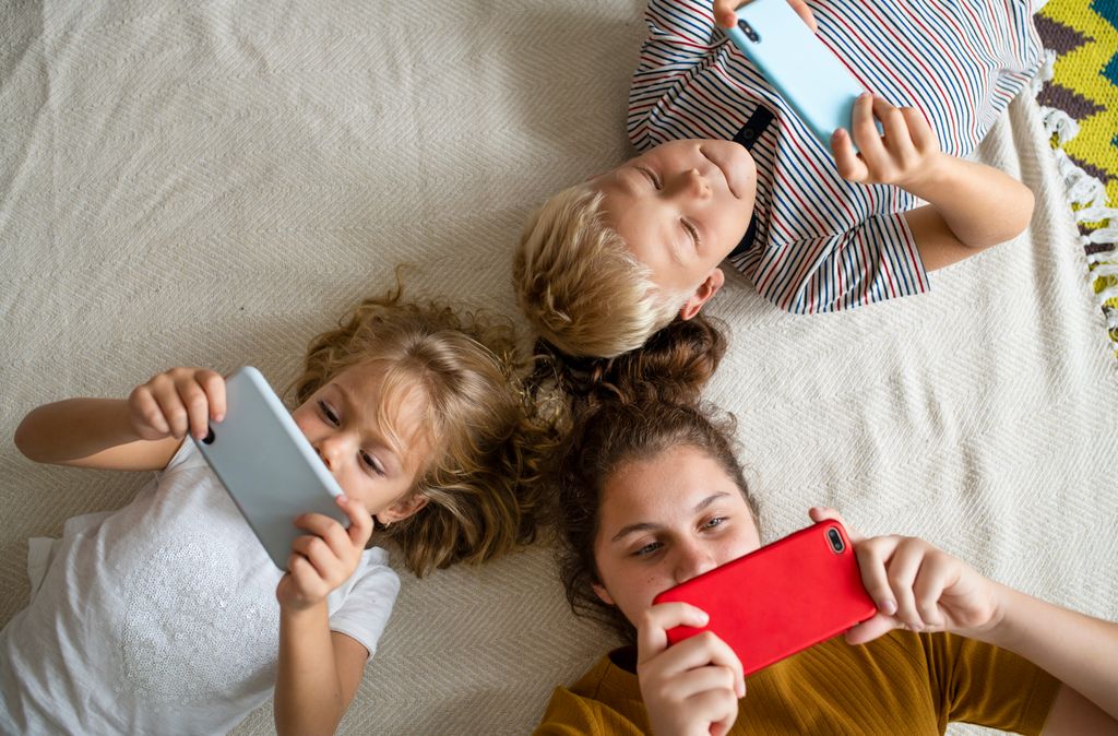 Niños tumbados en el suelo mirando sus teléfonos móviles