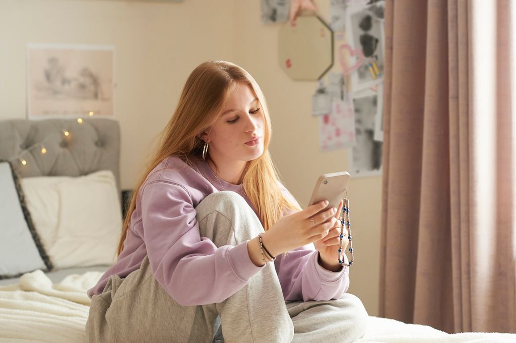 adolescente sentada en su cama mirando al móvil